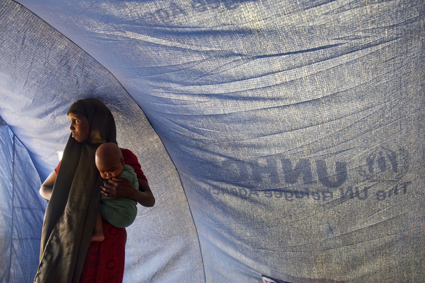 A Somali refugee stands inside a tent with her baby in Dollo Ado, Ethiopia.Fleeing drought and famine in their home country, thousands of Somalis have taken up residence across the border in Dollo Ado where a complex of camps is assisted by the UN Refugee Agency (UNHCR).